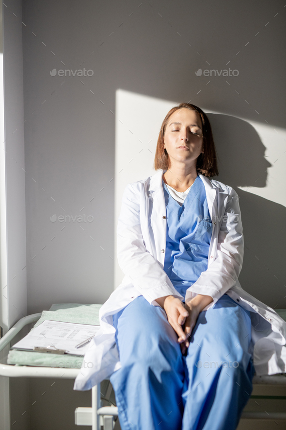 Exhausted nurse of hospital in whitecoat and uniform sitting on medical cart