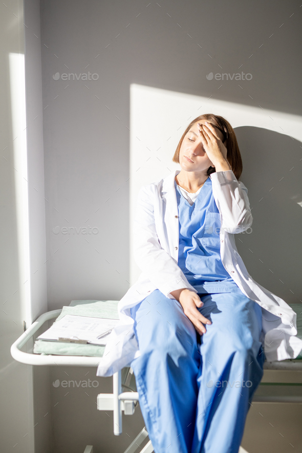 Exhausted nurse or assistant in whitecoat and uniform suffering from headache