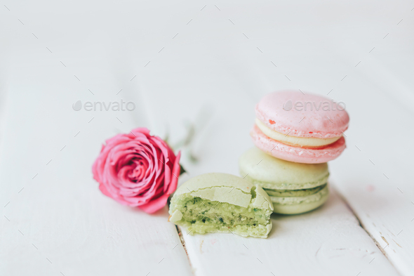 On a wooden background there are two macarons, one green and the other pink, and a beautiful rose