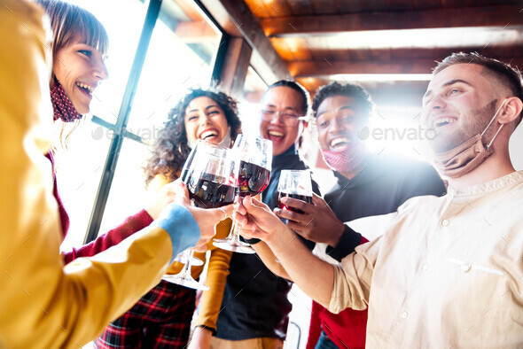 Happy friends wearing protective face masks toasting red wine at restaurant