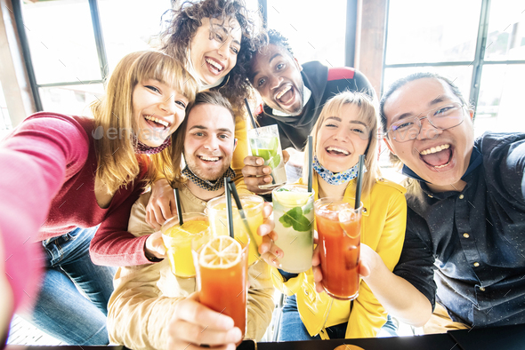 Multiracial people wearing protective face masks drinking cocktails at bar restaurant