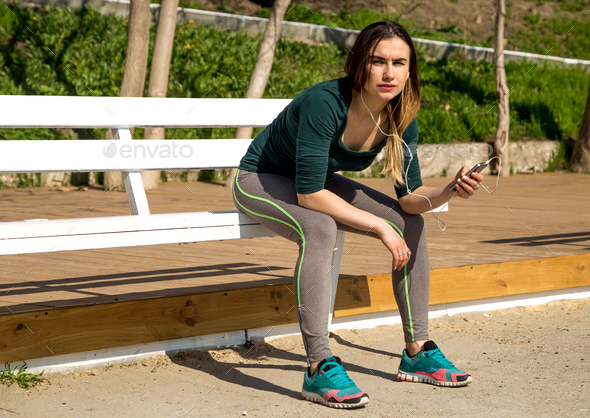 The girl in sportswear on a bench listening to music