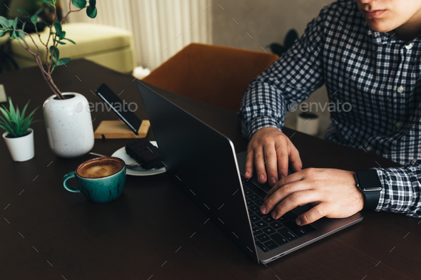 Man working at the laptop with a cup of coffee and chocolate cake, phone, plant