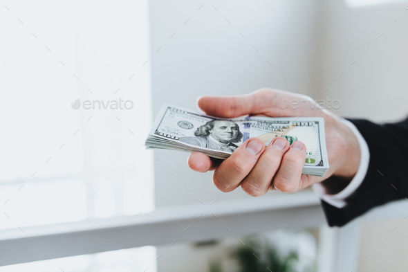 One hundred dollar bills money bundle, in hand of man in suit and white shirt