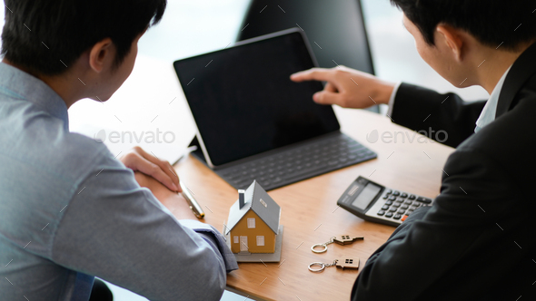 Bank staff with laptop recommending home loan, House model and calculator placed on the table.
