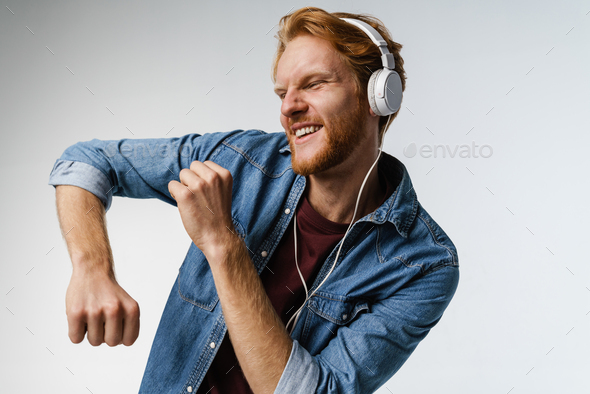 Happy handsome redhead guy in headphones singing and dancing