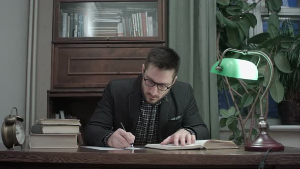 Concentrated Male Researcher Reading Book and Making Notes at the Desk