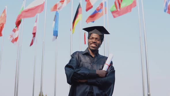 Happy Young African American Male Graduate Standing in Front of the Camera with a Diploma in His alt