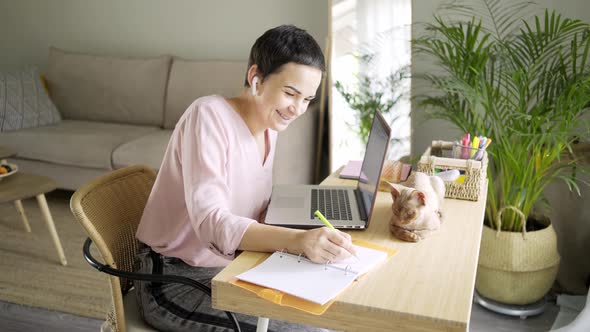 Woman Writes in Notebook at Table with Notebook and Cat