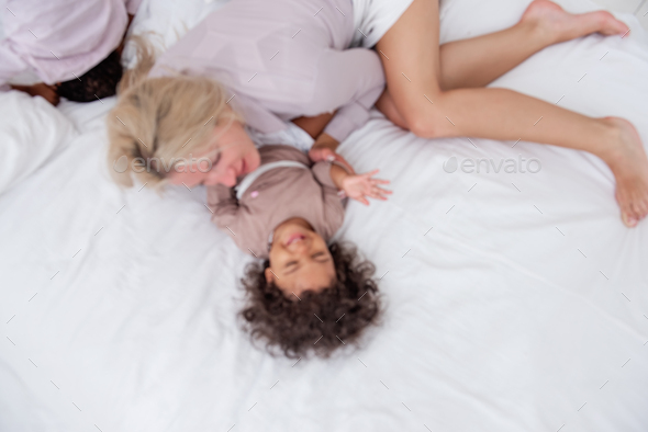 Defocused Young Caucasian blond mother tickles her little African American daughter having fun