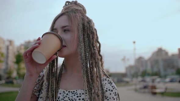 Young Girl with Dreadlocks with Coffee Walks on the Street