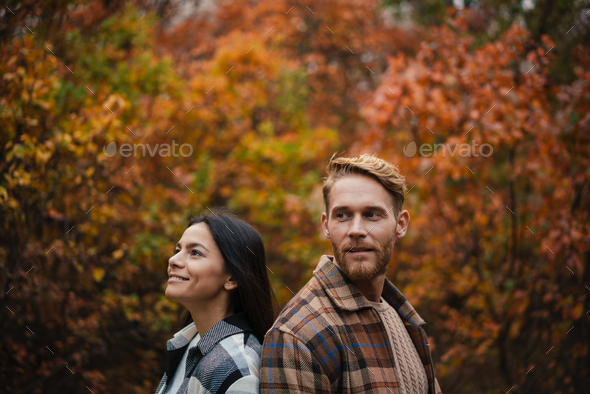 Beautiful happy couple smiling while standing back to back in forest