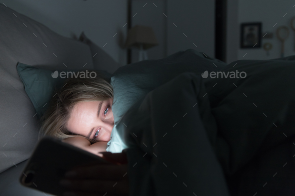Exhausted woman lying in bed using cellphone, chatting in social networks, can not sleep, insomnia.