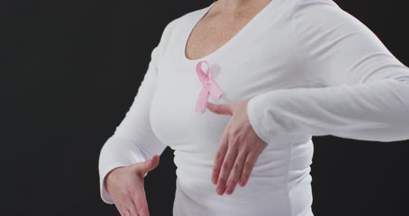 Mid section of a woman showing the pink ribbon on her chest against black background alt