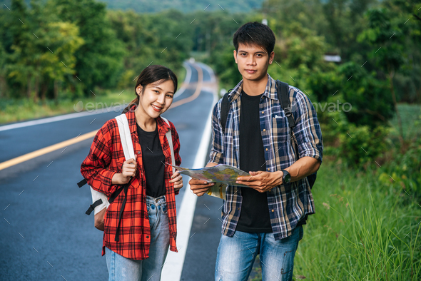Both male and female tourists stand to see the map on the road.