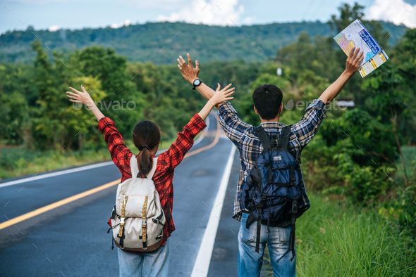 Both male and female tourists carry a backpack, stand on the road, raise their hands on both sides.