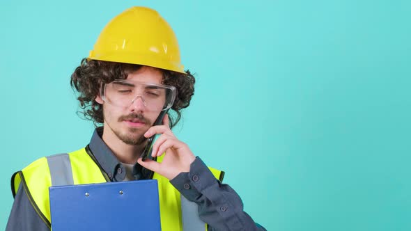 Construction Worker with Safety Glasses and Helmet That is Talking on Mobile Phone alt