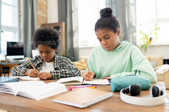 Clever and diligent girl and boy in casualwear making notes in copybooks