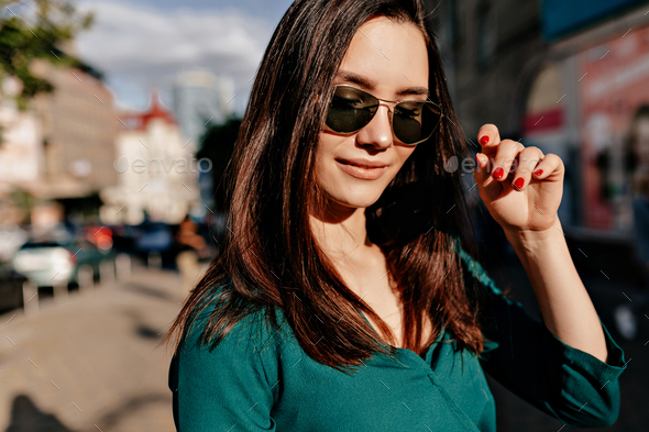 Outside portrait of charming european woman wearing black sunglasses and green blouse