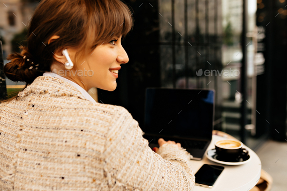 Close-up portrait from back of smiling happy woman dressed white jacket using headphones