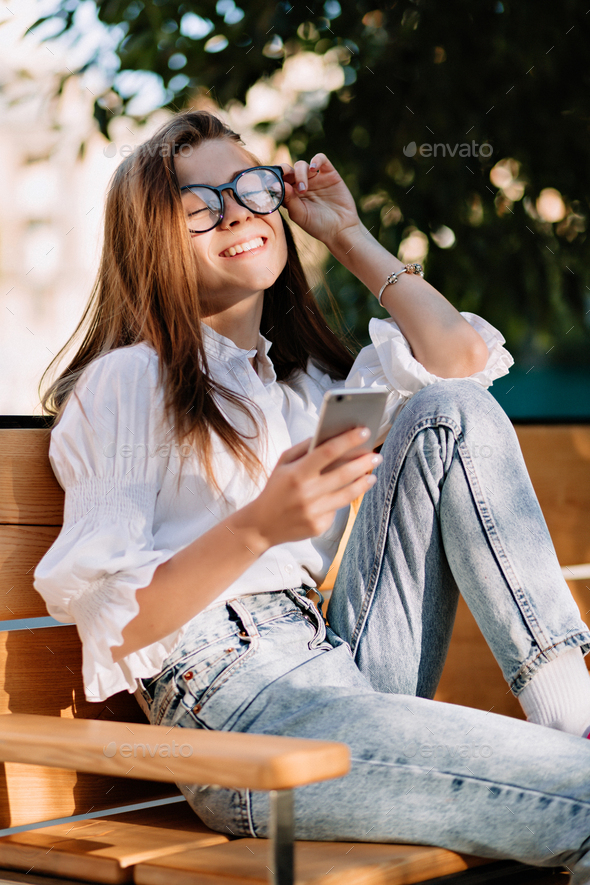 Happy charmnin g female student dressed white blouse and glasses sitting on open space