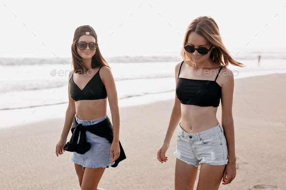 Young women wearing summer trendy outfits walking on the beach