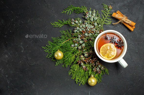 Overhead view of a cup of black tea xsmas accessories and cinnamon limes on black background