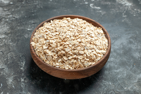 Front close view of organic oat bran in a brown wooden pot on dark background