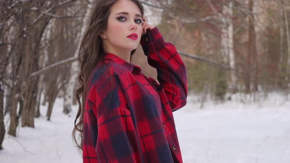 Young Woman with Wavy Hair Standing and Touching Face in Winter Forest