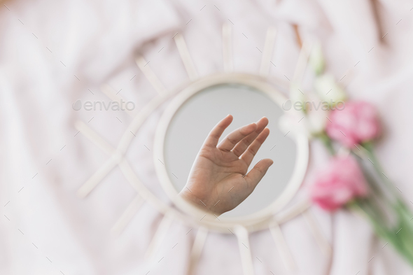 Hand reflected in mirror on background of soft fabric with eustoma flowers, aesthetic. Mental Health