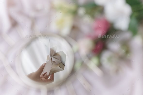 Hand holding gift reflected in mirror on soft fabric with flowers. Happy Women\'s and Mothers day