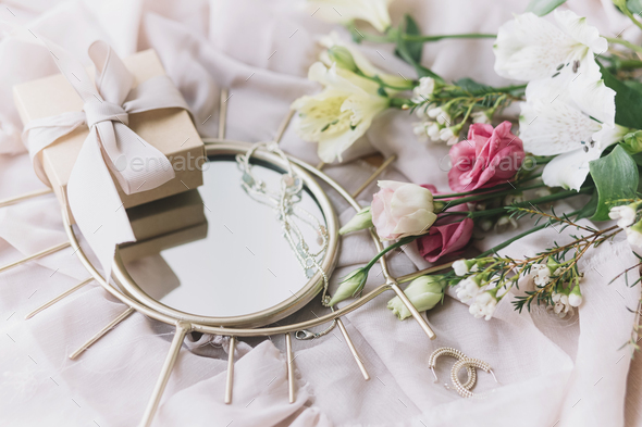 Stylish gift box, modern jewelry, spring bouquet on boho mirror on soft fabric. Happy Women's day