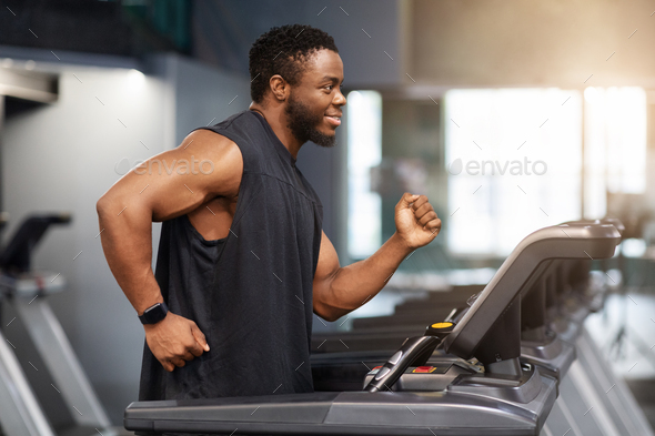 Motivated african american guy in black sportswear jogging at gym