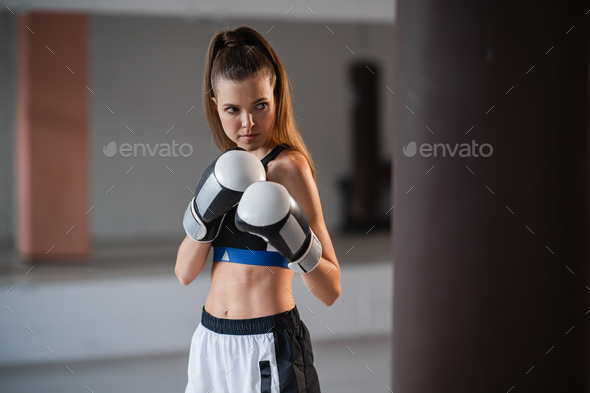 The girl is preparing for a boxing competition and trains punches on a punching bag in a spacious