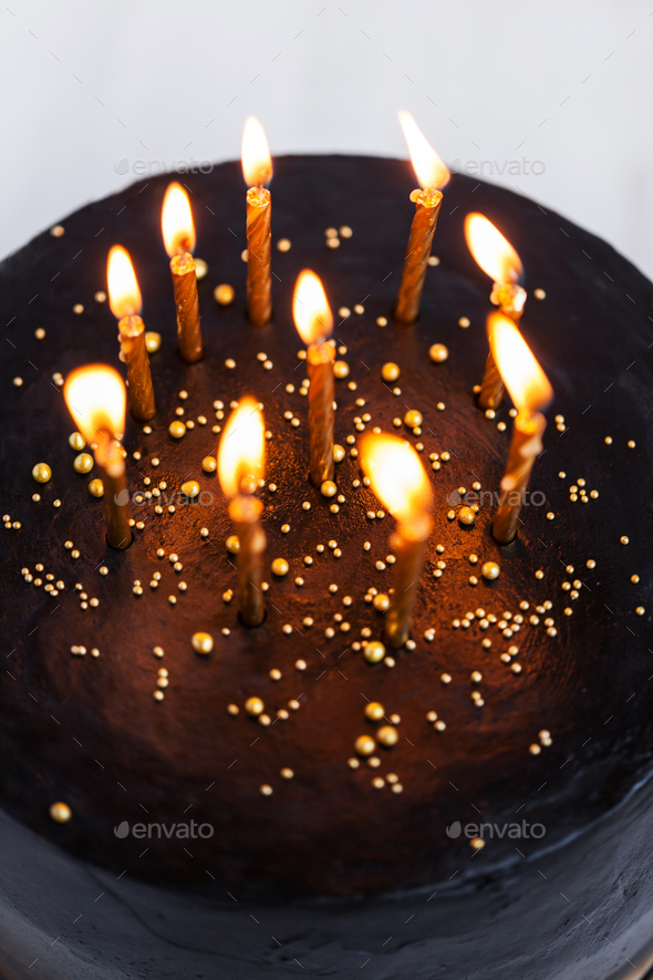 Black round birthday cake with burning golden candles on white background  Stock Photo by olegbreslavtsev