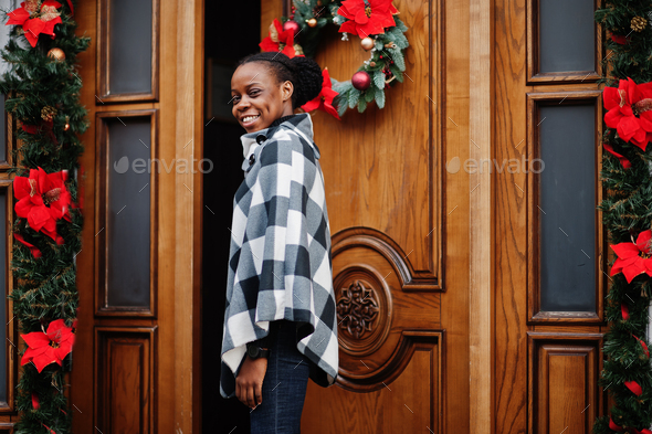African woman in checkered cape posed outdoor against christmas decorations.