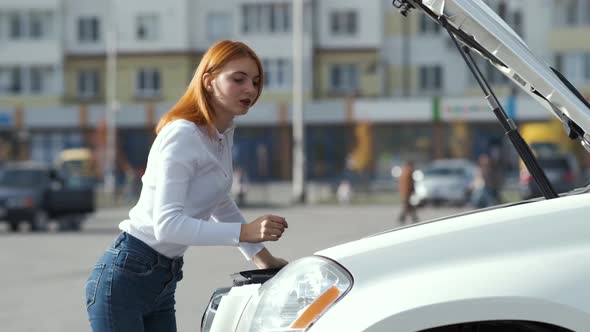 Young stressed woman driver near broken car with popped hood having a prbreakdown  alt