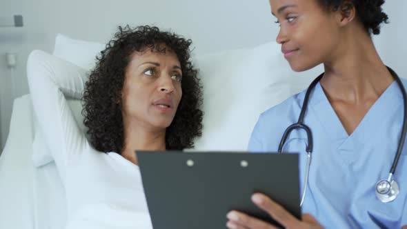 Front view of African american female doctor talking with female patient in the ward at hospital alt