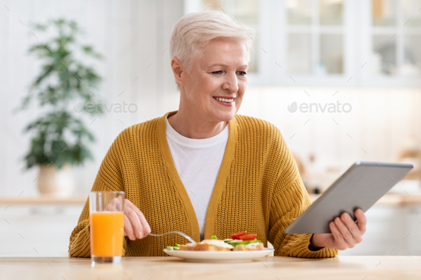 Joyful senior lady with digital tablet having lunch - Stock Photo - Images