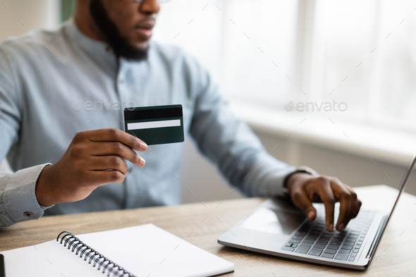 Black Businessman Paying Using Credit Card And Laptop In Office