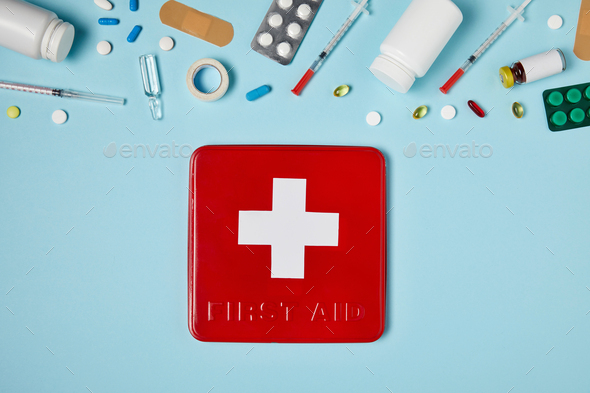 top view of red first aid kit box on blue surface with various medicines