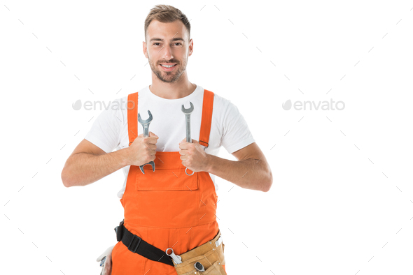 smiling handsome auto mechanic in orange uniform showing wrenches isolated on white
