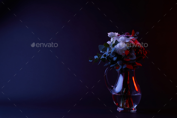 bouquet of different flowers in carafe with water on dark