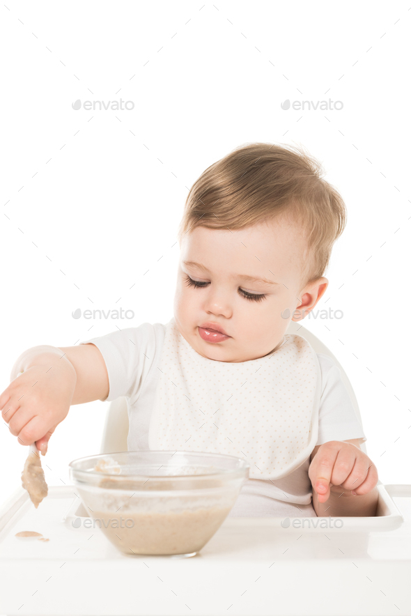 Baby boy in high chair eating pureed food with spoon - Stock Image