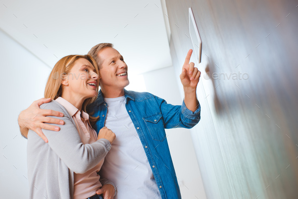 smiling man pointing at smart home control panel while hugging wife