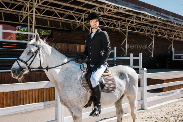 handsome male equestrian riding white horse at horse club