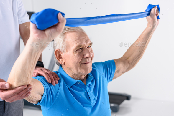 cropped shot of rehabilitation therapist assisting senior man exercising with rubber tape