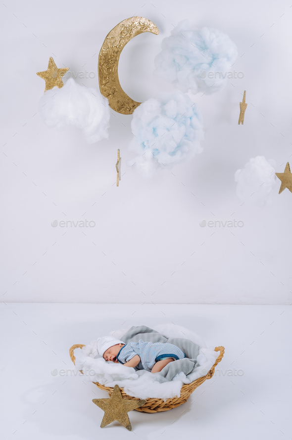 adorable newborn baby sleeping in basket with decorative clouds, moon and stars above head
