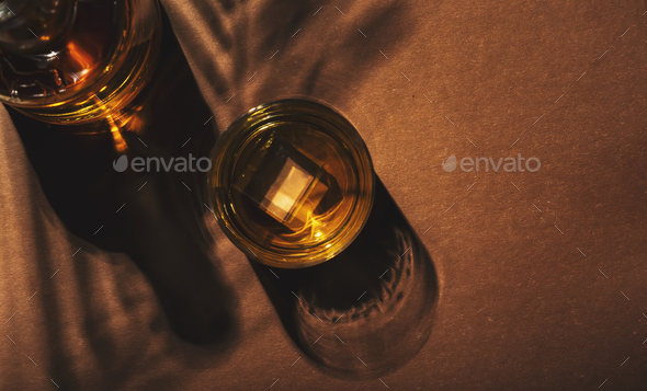 Contemporary still life with whiskey, scotch or bourbon glass with ice on textured brown background