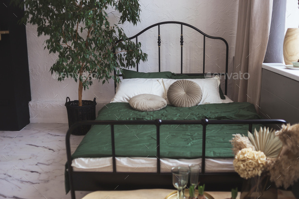 Light bedroom with black metal framed bed and home plant tree